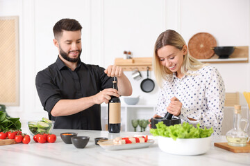 Smiling man opening bottle of wine while cooking with his wife at table in kitchen