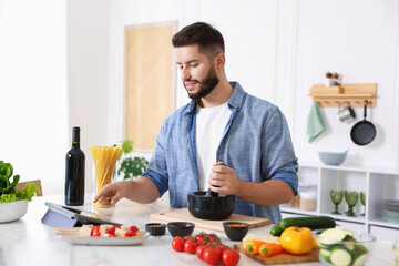 Smiling man looking at recipe on tablet while cooking at table in kitchen