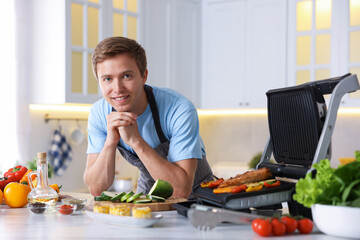 Man cooking vegetables and meat on electric grill in kitchen