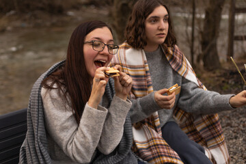 Two young women by the campfire eating sandwiches with cookies and marshmallows
