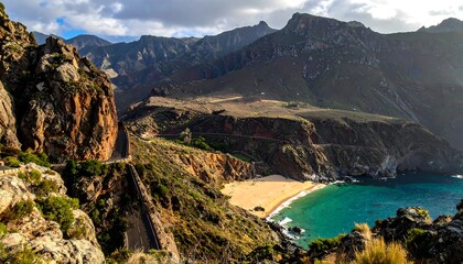 A coastal scene captures a sandy beach embraced by rugged cliffs and towering, textured mountains. Sunlight casts its glow across the serene turquoise water