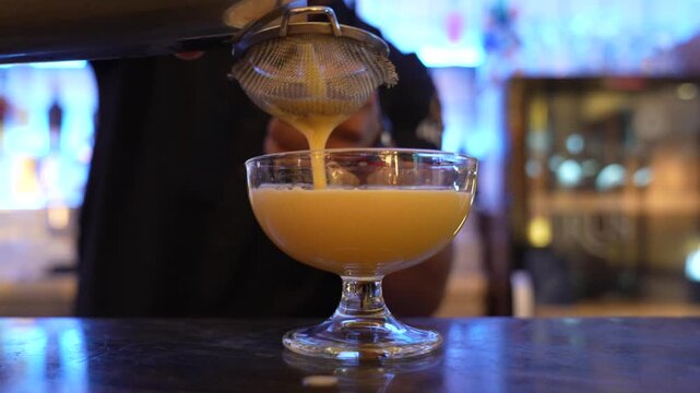 Bartender straining and pouring cocktail into glass