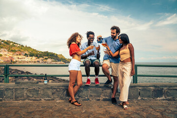 Diverse friends pouring amber craft beer, celebrating together on a summer vacation by the sea....