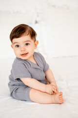 Fototapeta premium smiling baby on a white bed after sleeping, cute baby in a gray cotton bodysuit on a bed, space for text, baby boy