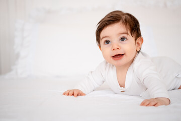 a baby on a white bed at home, a place for text, a cute smiling little child getting ready for bed, a portrait of a little boy child