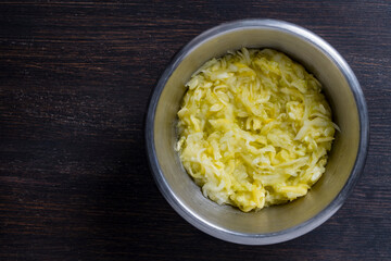 Grated zucchini in a metal bowl on a wooden table, closeup, top view, copy space. Raw materials for the preparation of vegetable waffles, pancakes. Food concept