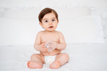 A baby in diapers on a white bed at home, a place for text, a cute smiling little child