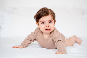 A crying baby on a white bed at home, a place for text