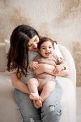 baby and mother, mom hugging baby at home, maternal love and care, mom with a small child, brown or beige background