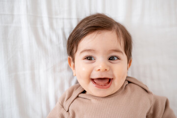 a baby, a close-up portrait of a smiling or laughing baby boy on a white bed, a place for text