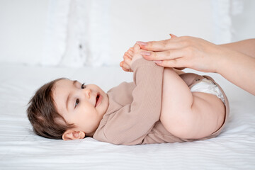 baby, mom holds the baby's legs on a white bed at home, maternal love and care