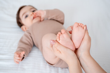baby's legs on a white bed, a place for text, mom's hands holding the baby's legs