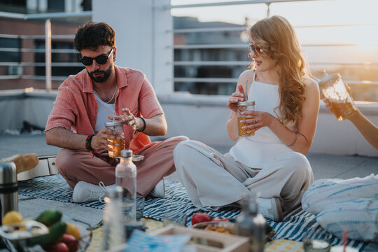Diverse friends socializing on a rooftop, enjoying beverages and the evening sun. - Powered by Adobe
