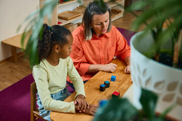 Teacher and child learning activity with focus on wooden cubes. Concept of child development,...