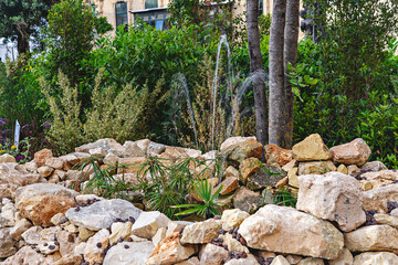 Textured stone and boulder arrangement with native plants forms dry garden exhibit within urban plaza under soft spring sky