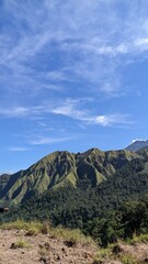 Obraz premium Scenic view of green mountains under a bright blue sky with soft clouds, perfect for travel, adventure, nature, and landscape backgrounds.
