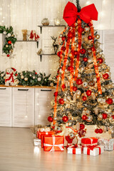 Christmas tree with New Year decor with red balls and gifts under it in the kitchen of the house, New Year's festive atmosphere at home