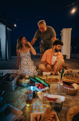 A casual rooftop gathering at night with friends enjoying food, conversation, and ambient string lights.