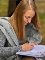 woman writes on a notebook in an autumn park