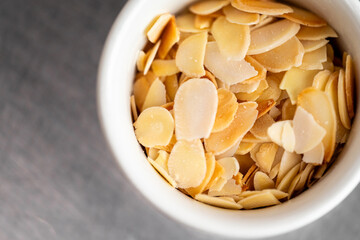Close-up of sliced almonds in a white ceramic bowl on a metal surface. Minimalist food styling, ideal for culinary, baking, or healthy eating themes.