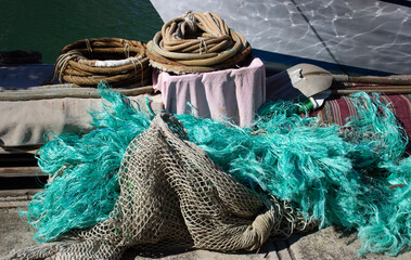Fishing gear on a dock near water: coiled ropes, turquoise net, pink towel, and striped mat. Rich textures and maritime colors evoke a vivid coastal atmosphere. Horizontal outdoor composition.
