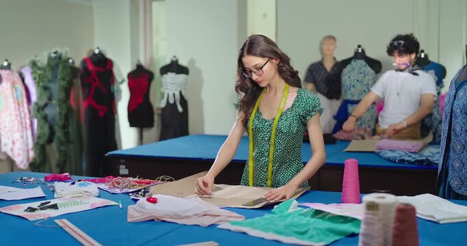 Indian young adult gen z lady female wear tape around neck learn clothe craft skill fashion design course. Smart pupil girl hold pencil do fabric paper pattern on desk new day college class room place