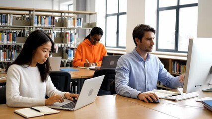 Students Using Laptops and Desktop Computer in Library - A diverse group of students are studying in a library. Some students are using laptops and desktop computers, while another is writing notes. - Powered by Adobe