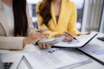 Asian business women professionals collaborate on financial data analysis reviewing reports discussing growth strategy in an office meeting workspace