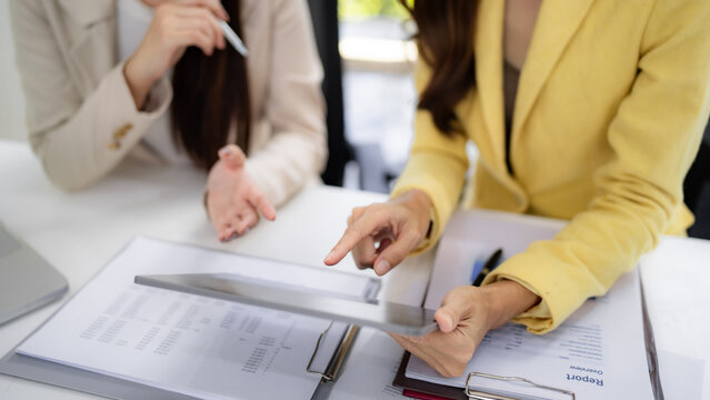 Adult Asian businesswomen analyze financial data collaborate on project discussing strategy in modern office setting