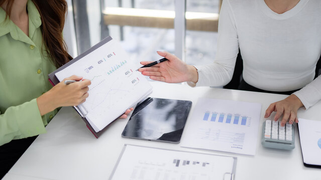 Adult Asian business women analyze financial data reports discussing growth strategy professional office meeting for project review