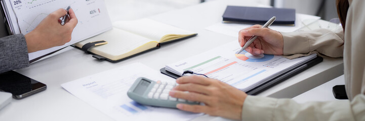 Business professionals analyze financial data reviewing budget reports using calculator and charts collaborating on strategic planning in a modern office workspace