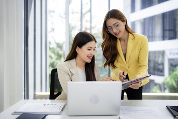 Asian adult businesswomen collaborate office laptop review documents analyze data discuss strategy modern workspace professional environment teamwork success