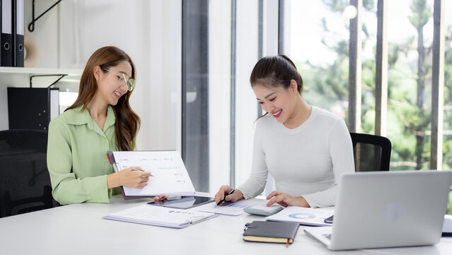 Adult Asian businesswomen discuss financial data analyzing reports planning strategy in modern bright office workspace collaborating teamwork professional environment