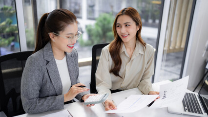Asian adult businesswomen collaborating office discussing financial reports analyzing data using calculator during project meeting planning strategy professional work