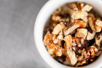 Close-up of chopped walnuts in a white bowl on gray background. Shelled nut pieces with natural texture and color. Ingredient for baking, cooking, or healthy snacking
