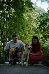 Obraz premium Happy couple crouching and petting their dog on a forest path. Outdoor activity with pets and love.