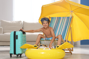 Dreaming about vacation at sea. Little boy with diving mask and flippers on deckchair near inflatable ring indoors © New Africa