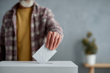 A close-up of a senior man with a light beard putting a paper ballot into a ballot box, symbolizing civic engagement and participation in elections
