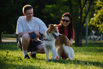 Happy couple petting their dog on the grass in the park at golden hour. Love, joy, and pets outdoors concept.