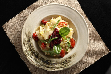 Overhead shot of gourmet pappardelle pasta with sun-dried tomatoes, roasted cherry tomatoes, basil, and red pesto, served on a rustic plate. Healthy and vegan meal.
