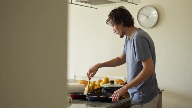 A young man is cooking food in the kitchen, focusing on preparing a delicious homemade meal. A relatable and warm moment of homemaking, creativity, and culinary enjoyment in a cozy setting.