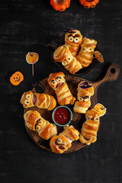 Naklejki Halloween food. Scary sausage mummies in dough with funny eyes on dark background. Funny decoration. Top view