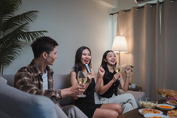 Asian friends enjoying home karaoke party celebrating friendship