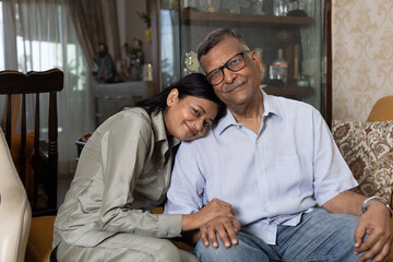 Obraz premium Indian happy daughter hugging and sit with older father. Attractive woman daughter sitting on sofa with father. senior mature man in house, enjoy spend time together in living room. Happy Fathers day