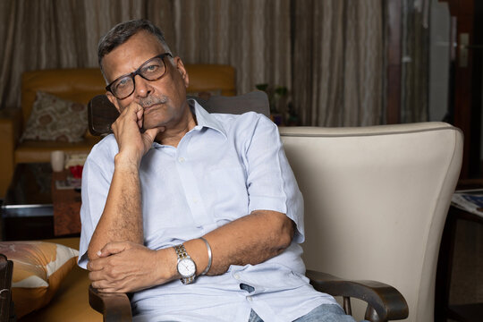 Thoughtful Senior man rest on sofa at home feel sad while sitting on sofa. Indian Pensive elderly 60s man sit relax on couch in living room Concept of sad senior citizen.