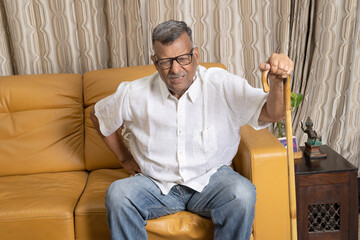 Happy senior man talking on mobile phone looking aside sitting on couch at home. Old male modern  communicating having cellphone conversation indoor. 