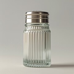 Classic Fluted Glass Salt Shaker with Polished Chrome Cap: This clean, minimalist studio shot captures a traditional, clear glass salt shaker filled with white seasoning, featuring vertical fluting an