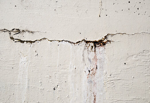 Vertical crack in concrete wall with water seepage. Outdoor wall damage with rust, efflorescence, moisture and discoloration. Structural defect or foundation problem from water. Selective focus.