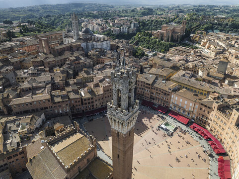Aerial view of Piazza del Campo's unique shell shape highlighted by the Torre del Mangia's imposing presence among the terracotta rooftops, Siena, Tuscany, Italy.
