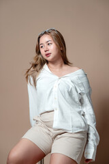 Obraz premium Asian Indonesian woman in a white shirt and beige shorts sitting with natural expression, confident pose, modern hairstyle, and stylish look, symbolizing beauty and lifestyle concept.